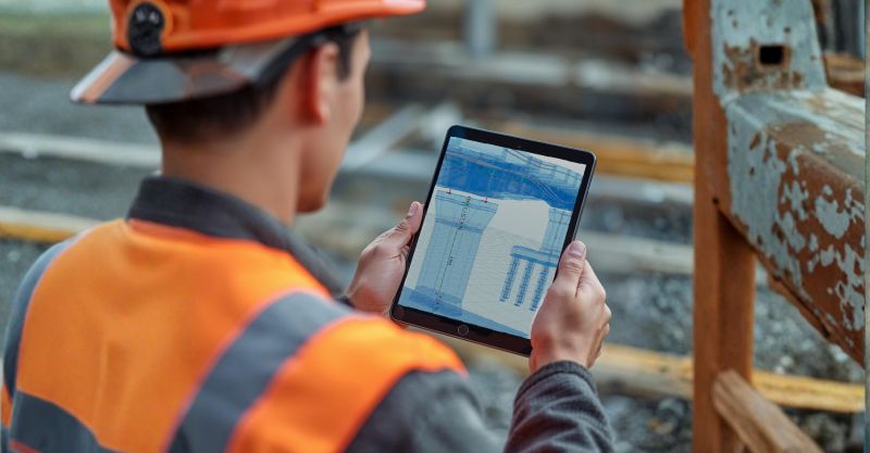 Construction manager using a tablet to review 4D BIM model and time-based project schedule at an active construction site in the USA